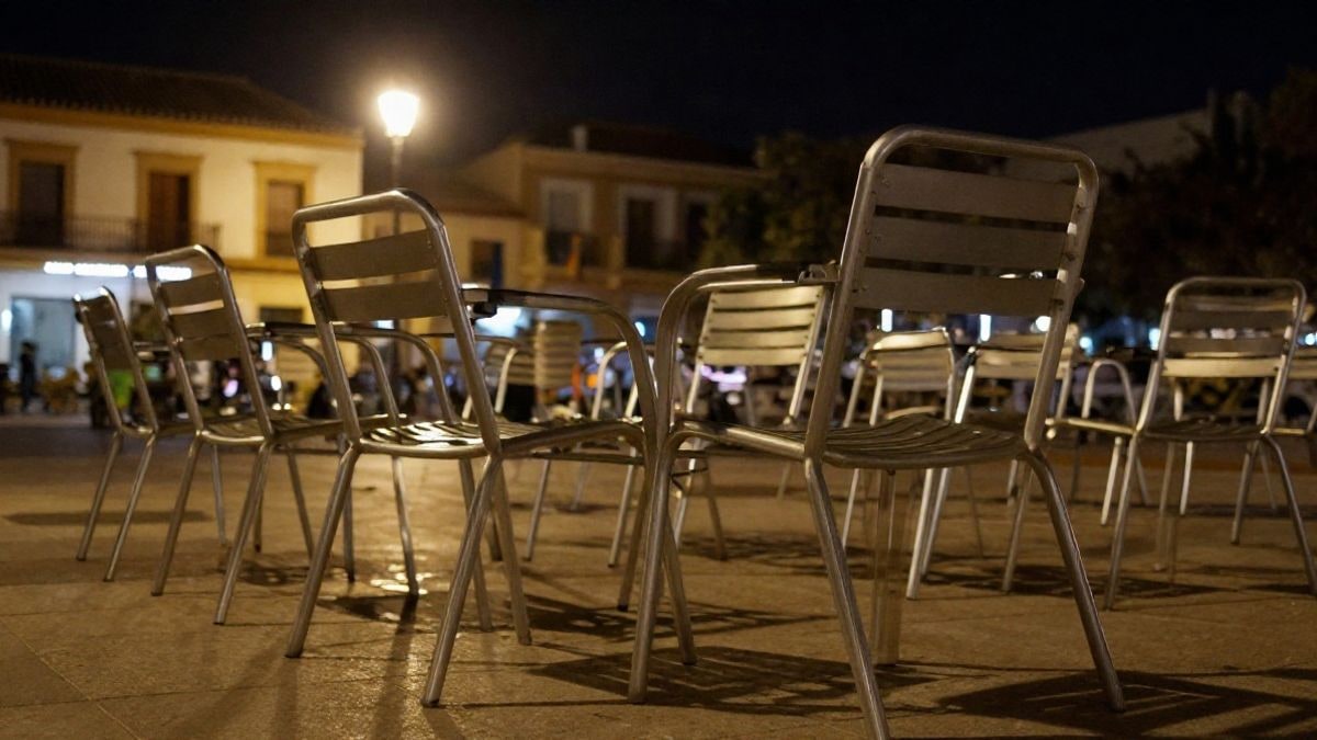 Imagen ilustrativa: sillas metálicas vacías en una plaza española iluminada por una farola durante la noche