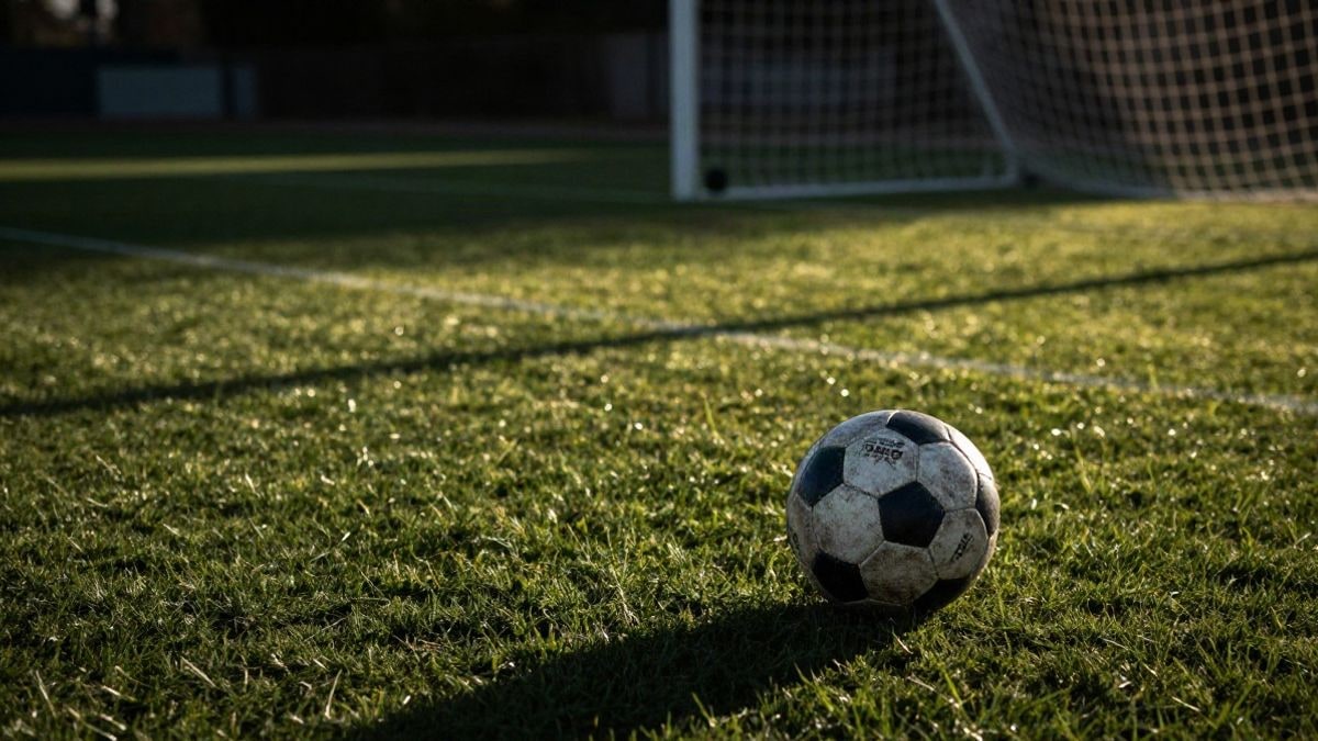 Imagen ilustrativa: balón de fútbol sobre el césped de un campo de entrenamiento al atardecer