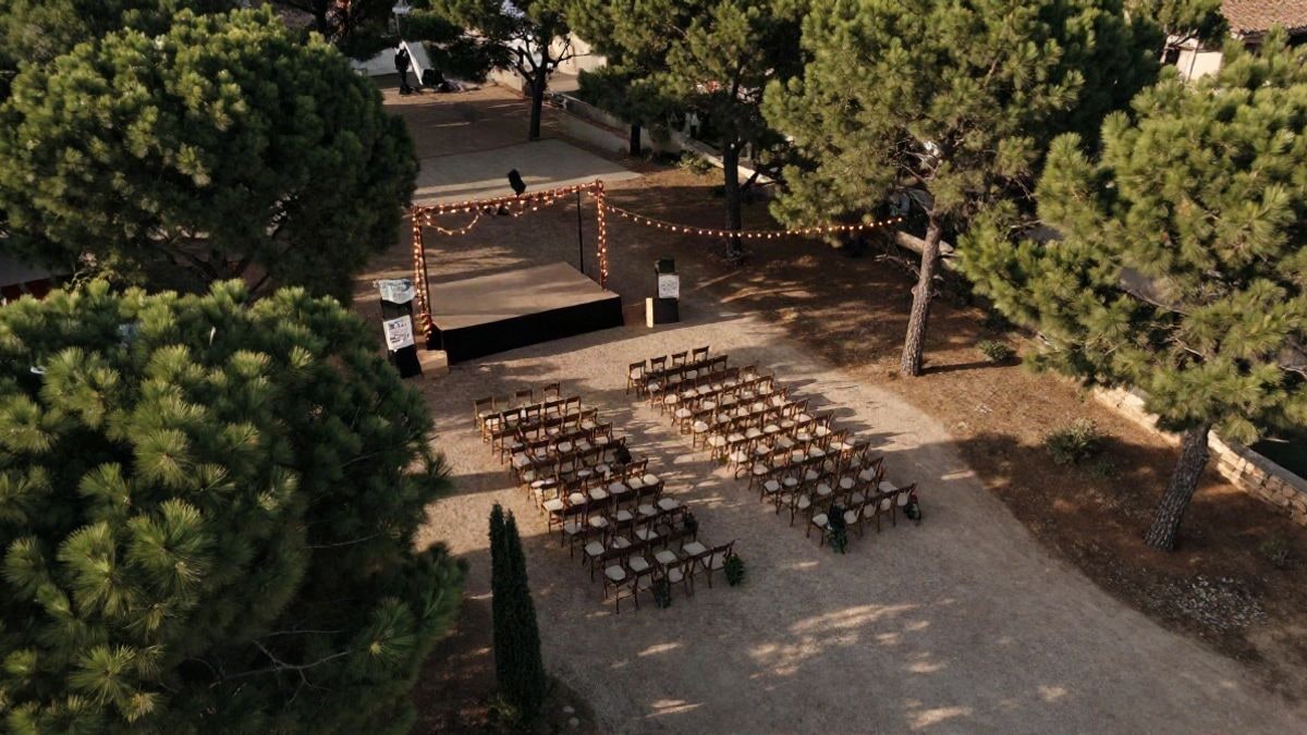 Imagen ilustrativa: vista cenital de un recinto al aire libre con sillas vacías y un escenario iluminado entre pinos