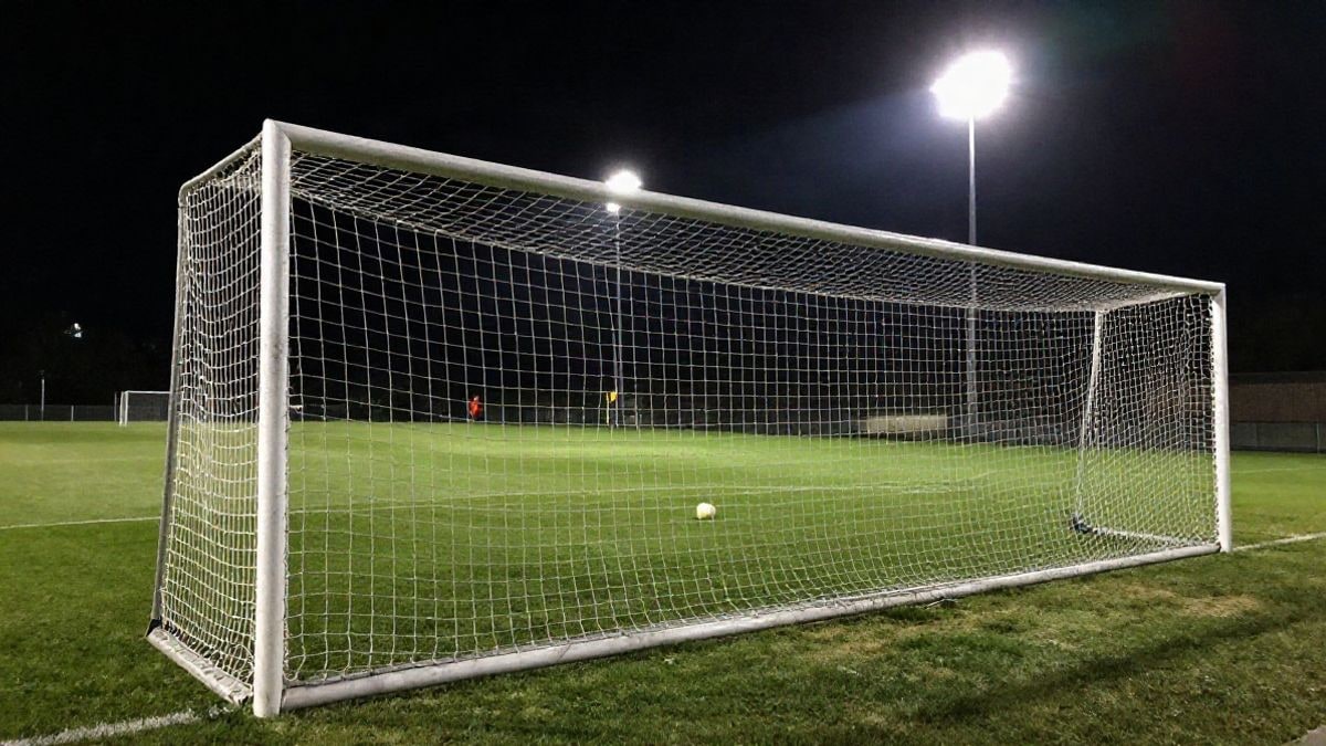 Imagen ilustrativa: campo de fútbol genérico iluminado por focos nocturnos, con la portería y la red en silueta