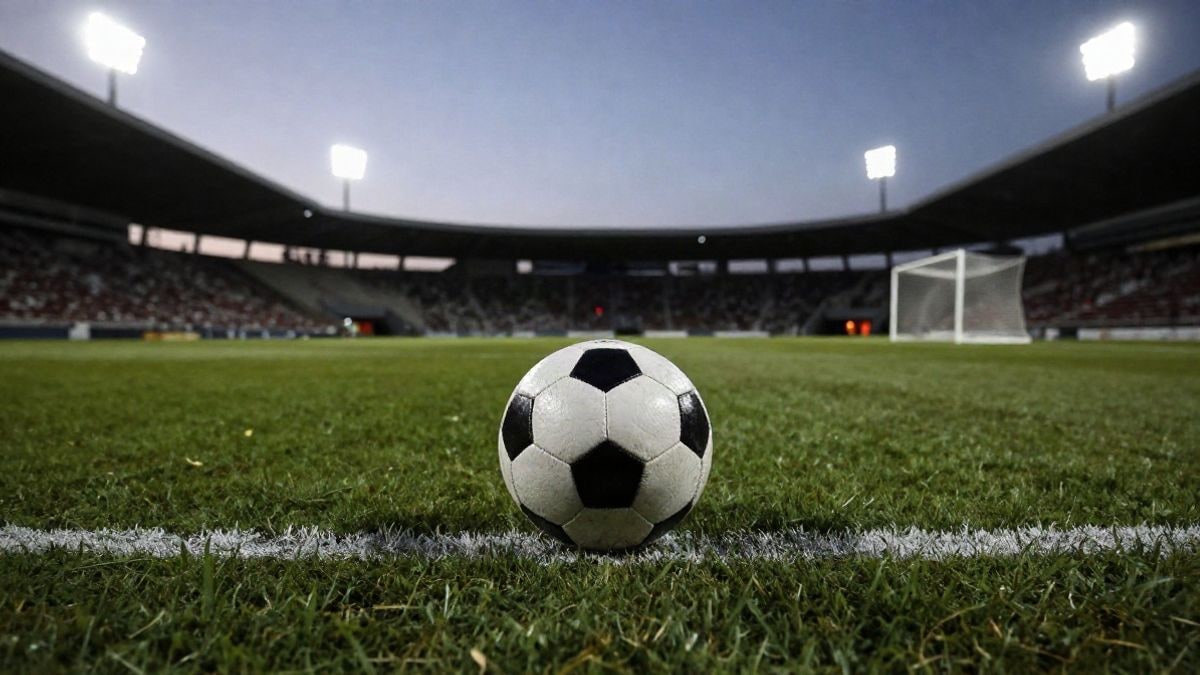 Imagen ilustrativa: balón de fútbol en el centro del campo de un estadio al atardecer, con las luces encendidas y una portería desenfocada al fondo