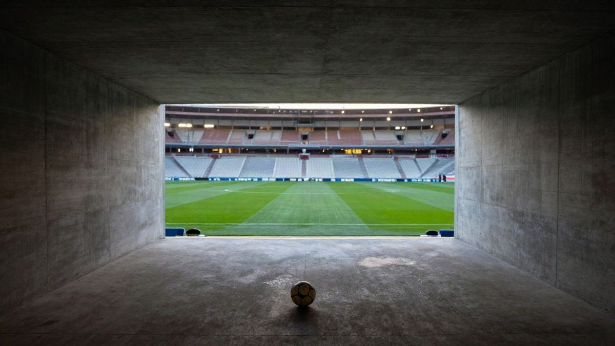 Imagen ilustrativa: túnel largo de un estadio de fútbol vacío al atardecer, con un balón en el suelo y luz natural suave