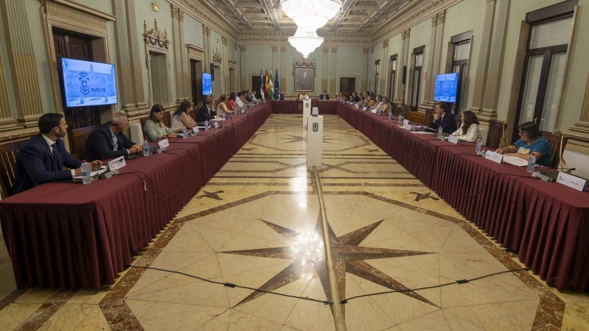 Imagen ilustrativa: sala de plenos municipal vacía con luz de atardecer entrando por las ventanas