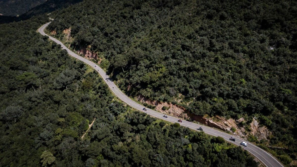 Imagen ilustrativa: vista aérea de una carretera de montaña con un pelotón ciclista y vehículos de apoyo en la provincia de Huelva.