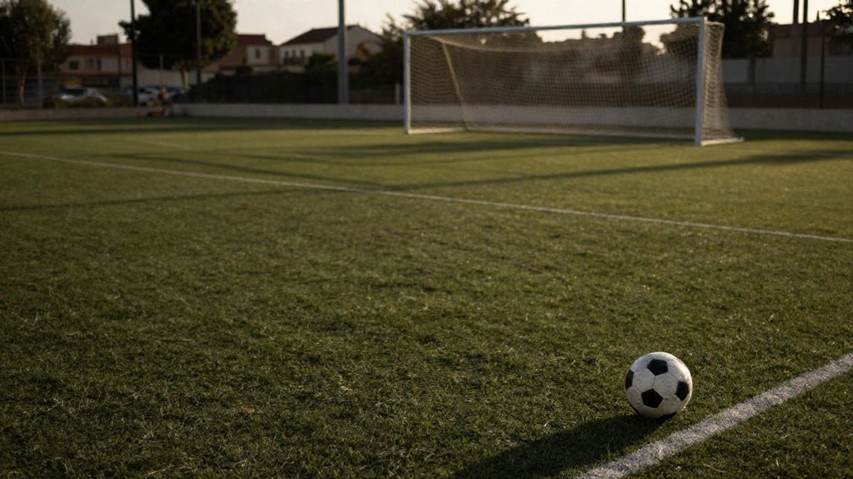 Imagen ilustrativa: un campo de fútbol municipal al atardecer con un balón sobre el césped y la portería al fondo