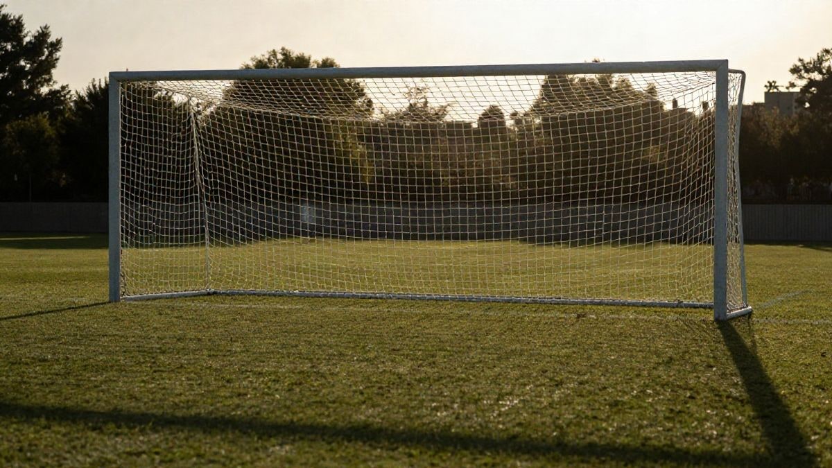 Imagen ilustrativa: portería de fútbol con red a contraluz al atardecer y sombras largas sobre el césped