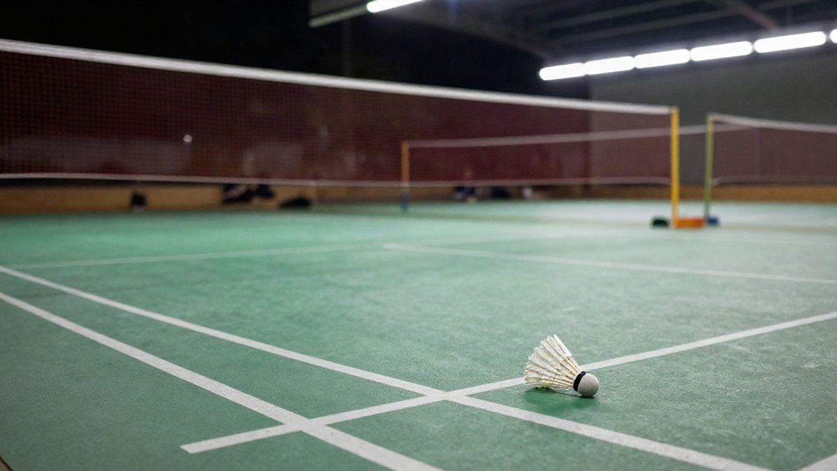 Imagen ilustrativa: pista de bádminton iluminada por focos, con un volante en el suelo junto a la red