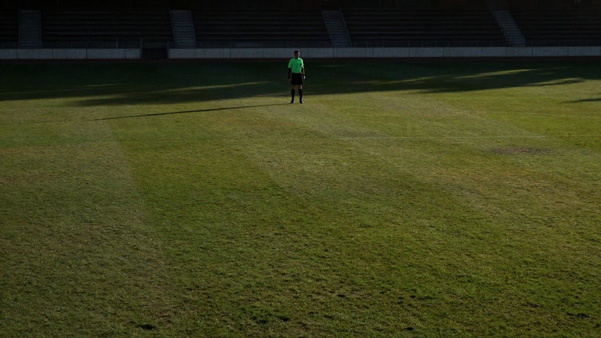 Imagen ilustrativa: campo de fútbol al atardecer con un árbitro solitario en la distancia y amplio espacio negativo
