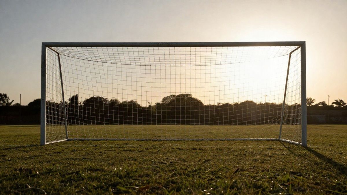 Imagen ilustrativa: portería de fútbol con red a contraluz al atardecer, sombras largas sobre el césped