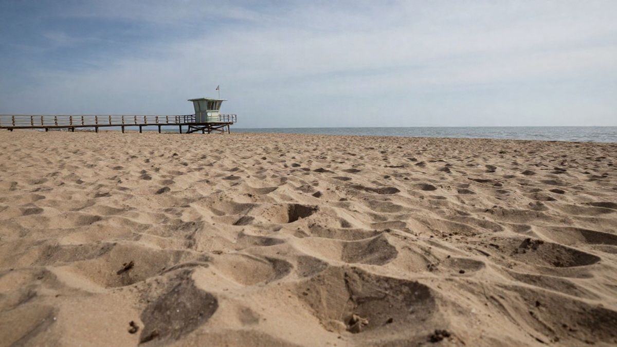 Imagen ilustrativa: ángulo bajo de una playa de arena con mar en calma y una torre de salvamento al fondo