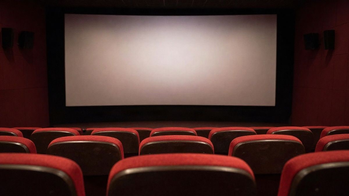 Imagen ilustrativa: sala de cine vacía con butacas rojas frente a una pantalla iluminada