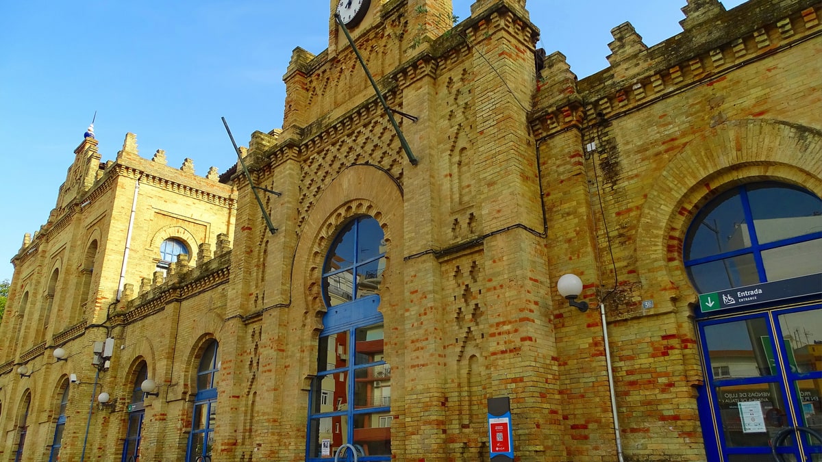 Fachada de ladrillo amarillo de la estación de tren de Huelva con reloj y entrada azul