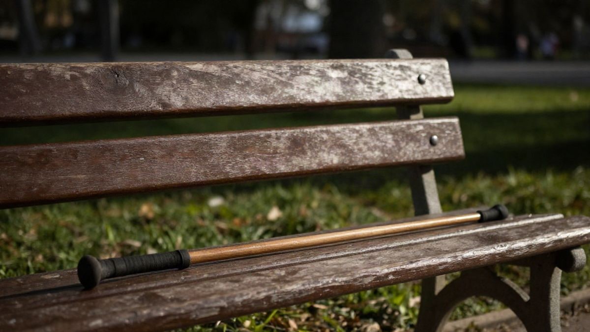Imagen ilustrativa: un banco de madera en un parque con un bastón apoyado, luz de tarde