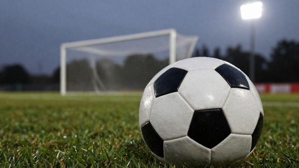 Imagen ilustrativa: primer plano de un balón de fútbol sobre el césped con una portería desenfocada al fondo