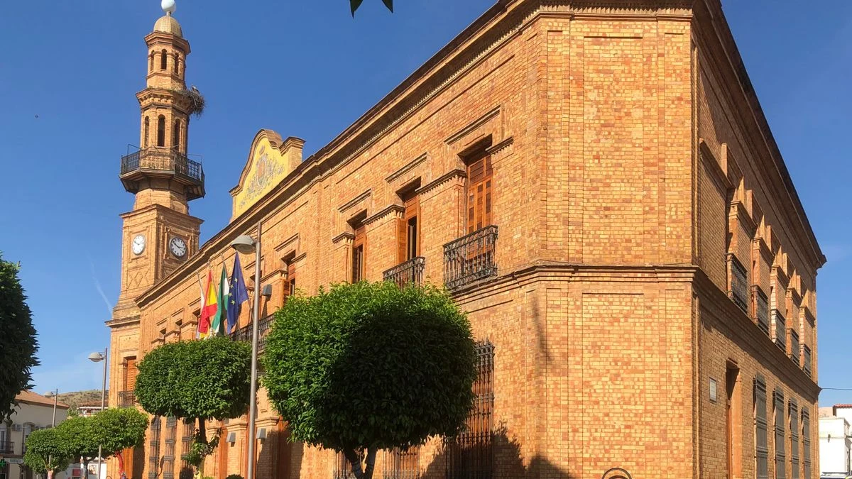 Imagen ilustrativa: calle de un pueblo minero al atardecer con charcos y una fachada municipal al fondo, tras las lluvias.