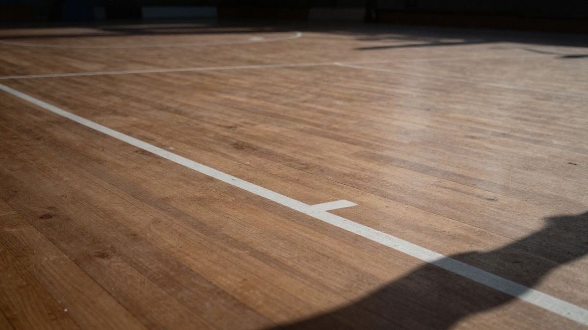 Imagen ilustrativa: suelo de madera de una pista de baloncesto con líneas blancas, visto desde ángulo bajo con cielo de fondo