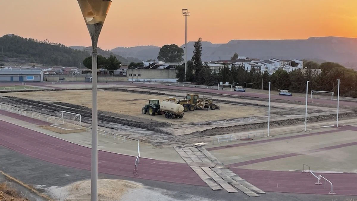 Imagen ilustrativa: campo de fútbol con césped artificial parcialmente instalado bajo focos, con maquinaria de obra.