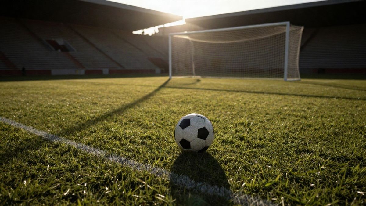 Imagen ilustrativa: un balón de fútbol sobre el punto de penalti de un estadio al atardecer, con sombras largas y la red de la portería al fondo.