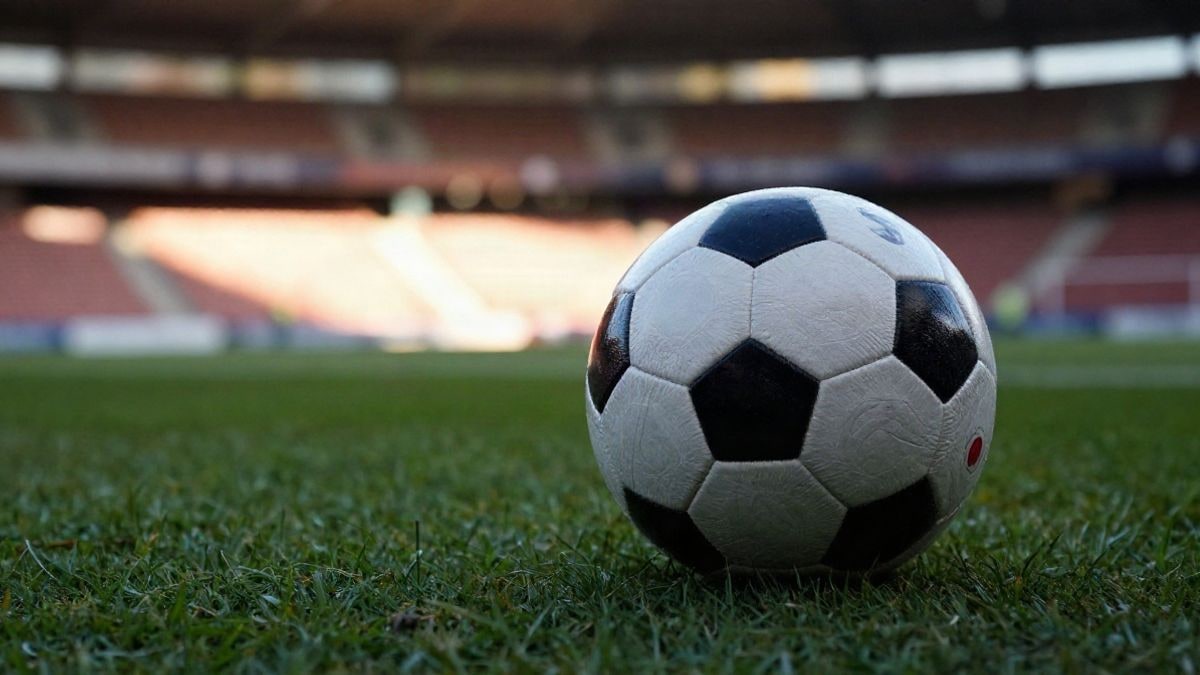 Imagen ilustrativa: un balón de fútbol sobre el césped de un estadio al atardecer, con las gradas de fondo desenfocadas.