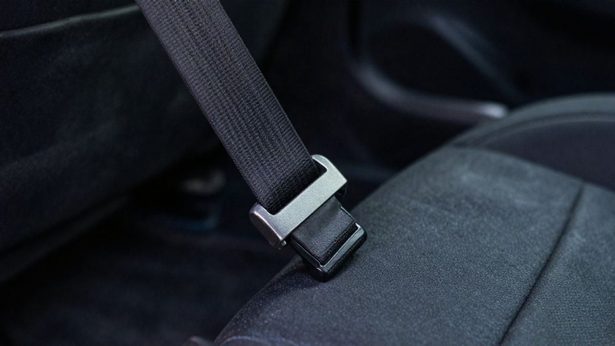 Imagen ilustrativa: un cinturón de seguridad abrochado sobre un asiento de coche oscuro, con luz lateral que crea sombras.