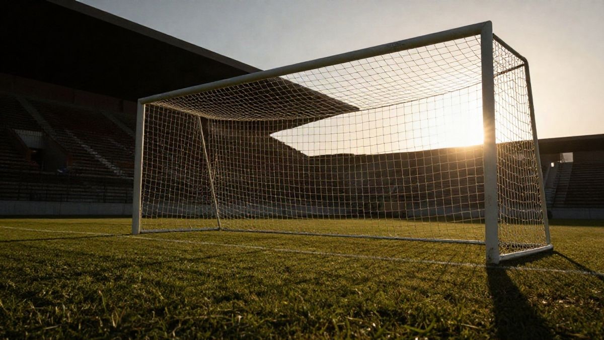 Imagen ilustrativa: portería de fútbol con la red a contraluz al atardecer y sombras largas sobre el césped