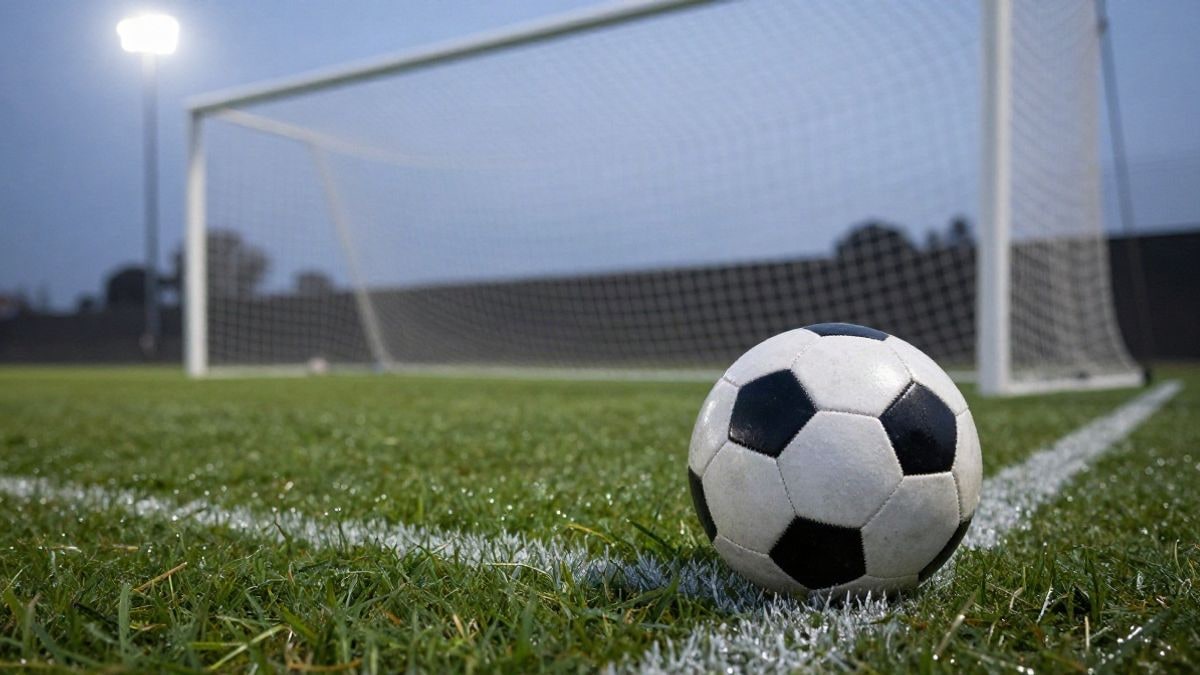 Imagen ilustrativa: balón de fútbol en el césped junto al banderín de córner, con la portería desenfocada al fondo