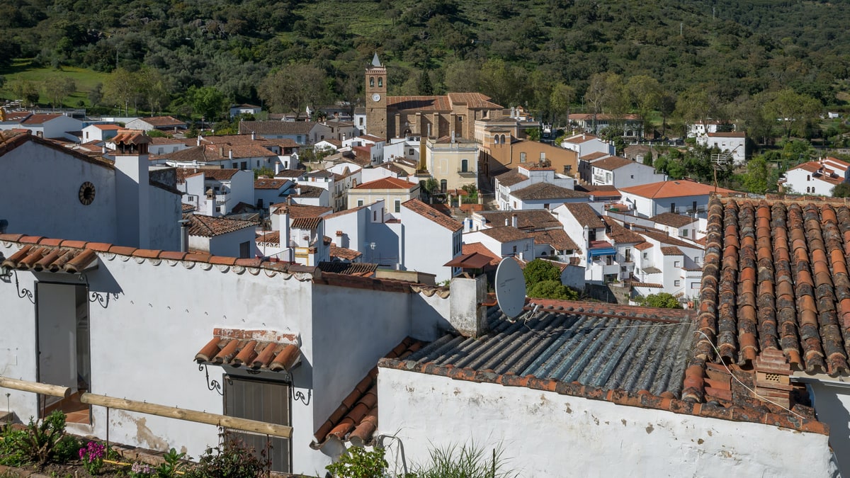 Vista panorámica de casas blancas y tejados del pueblo, con la torre de la iglesia y la sierra al fondo.