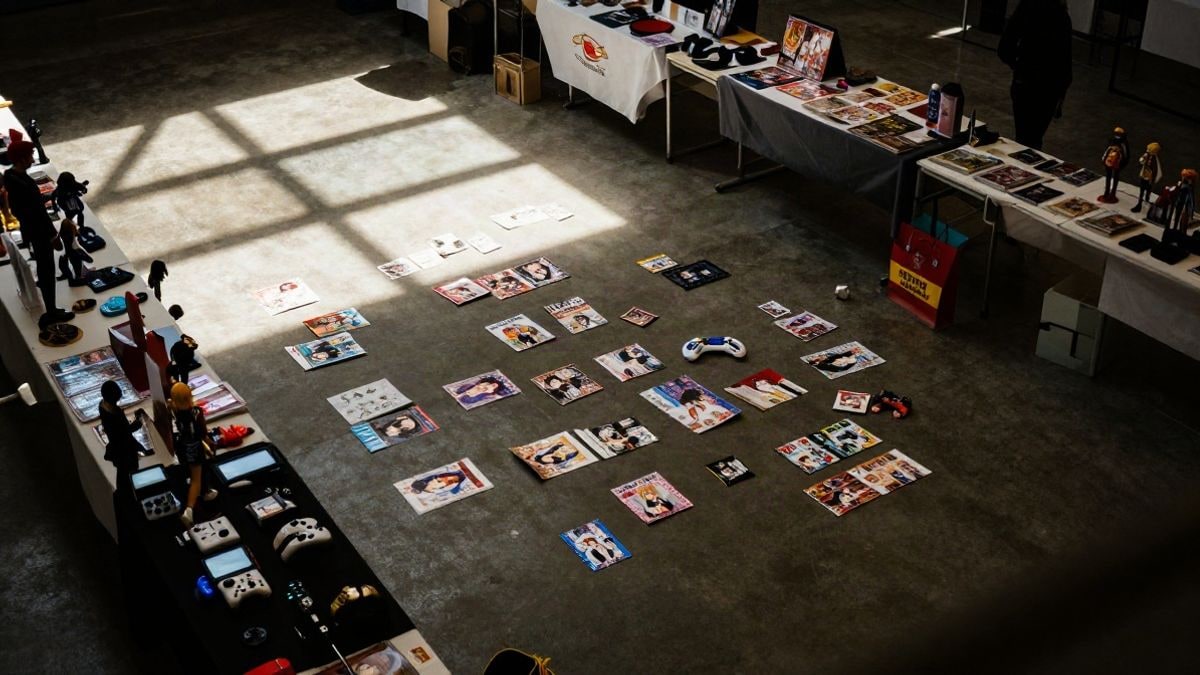 Imagen ilustrativa: vista cenital de una sala de convenciones con cómics, figuras y accesorios de videojuegos sobre mesas