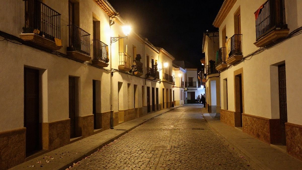 Imagen ilustrativa: calle empedrada iluminada con faroles y pétalos en el suelo, ambiente de procesión nocturna.