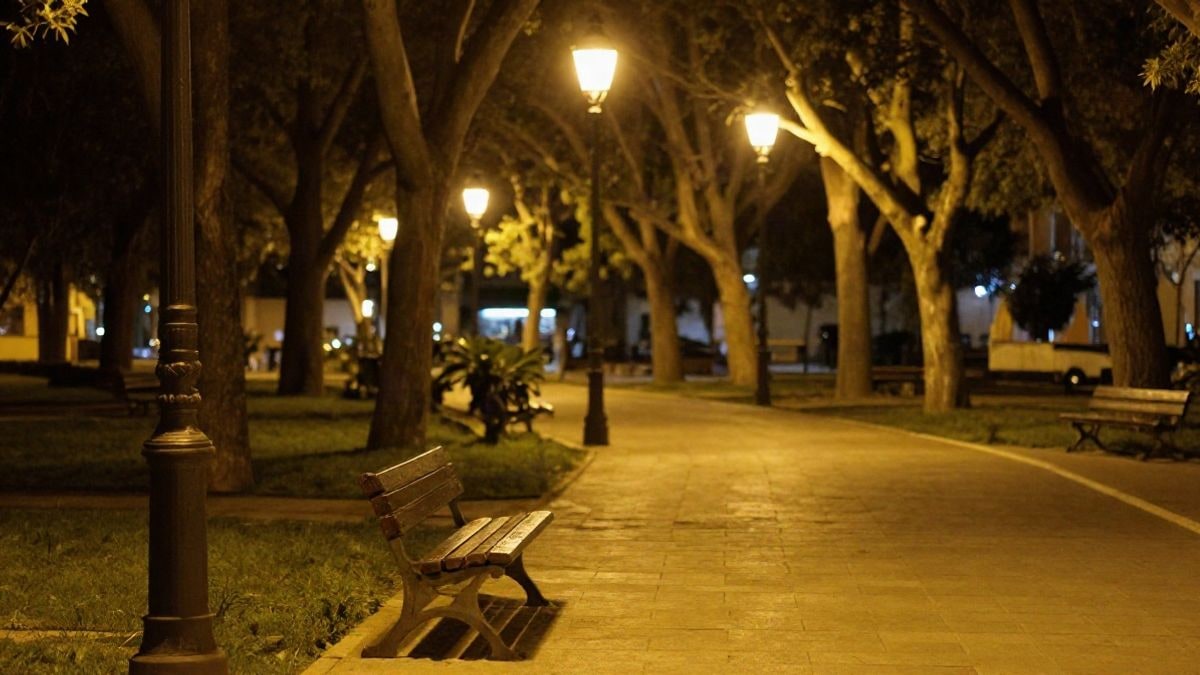 Imagen ilustrativa: paseo de piedra en un jardín público iluminado por farolas de luz cálida durante la noche