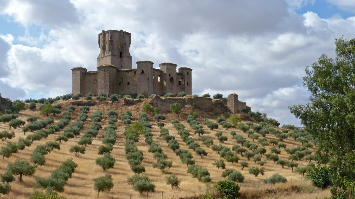 Castillo de Belalcázar sobre una colina con hileras de olivos y nubes de tormenta.