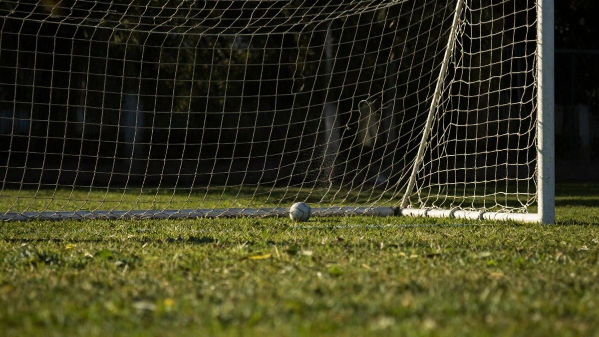 Imagen ilustrativa: red de portería de fútbol con un balón en su interior bajo la luz del atardecer