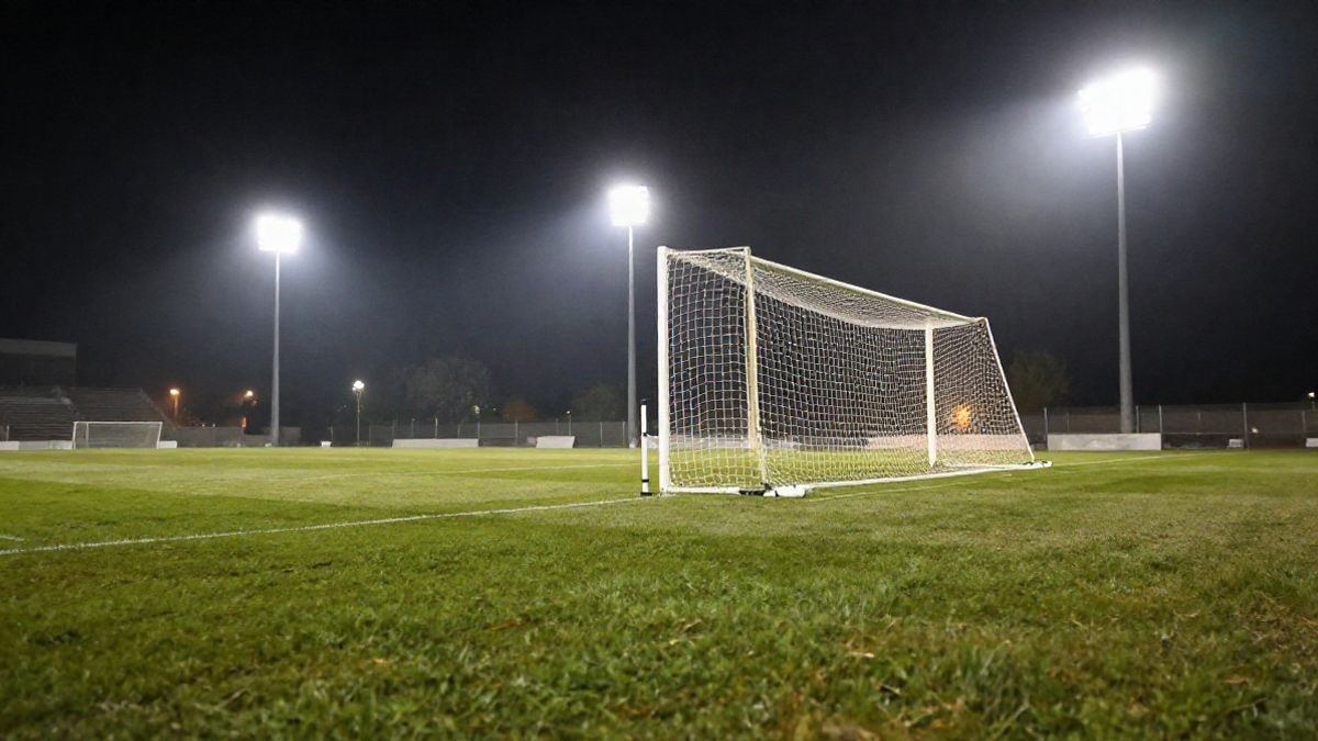 Imagen ilustrativa: focos de un estadio de fútbol encendidos de noche sobre un campo de hierba y una portería con red