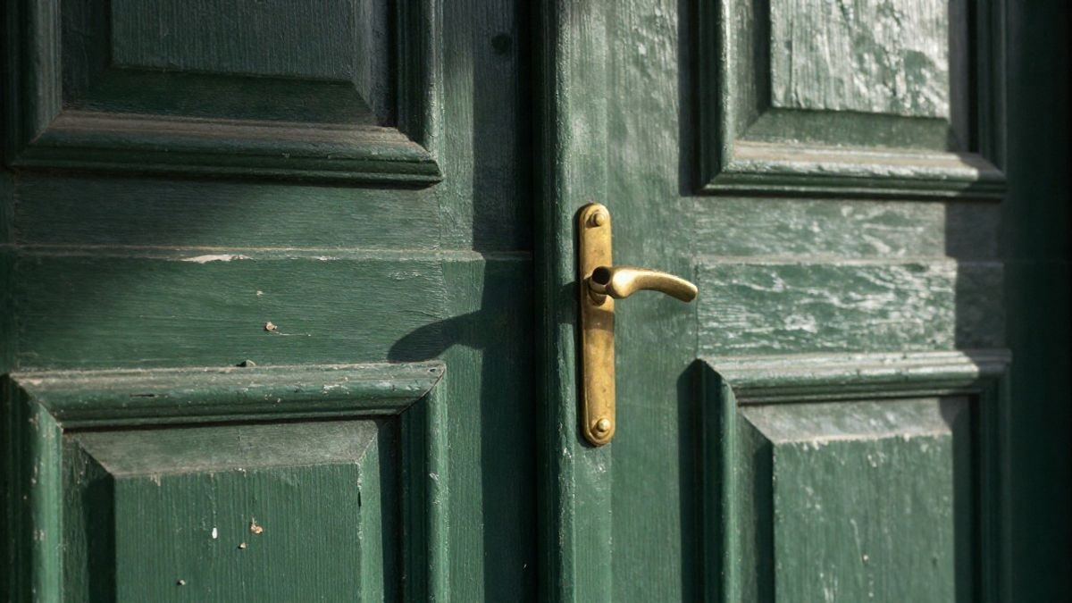 Imagen ilustrativa: detalle de una puerta de madera envejecida con pintura desconchada y luz natural suave