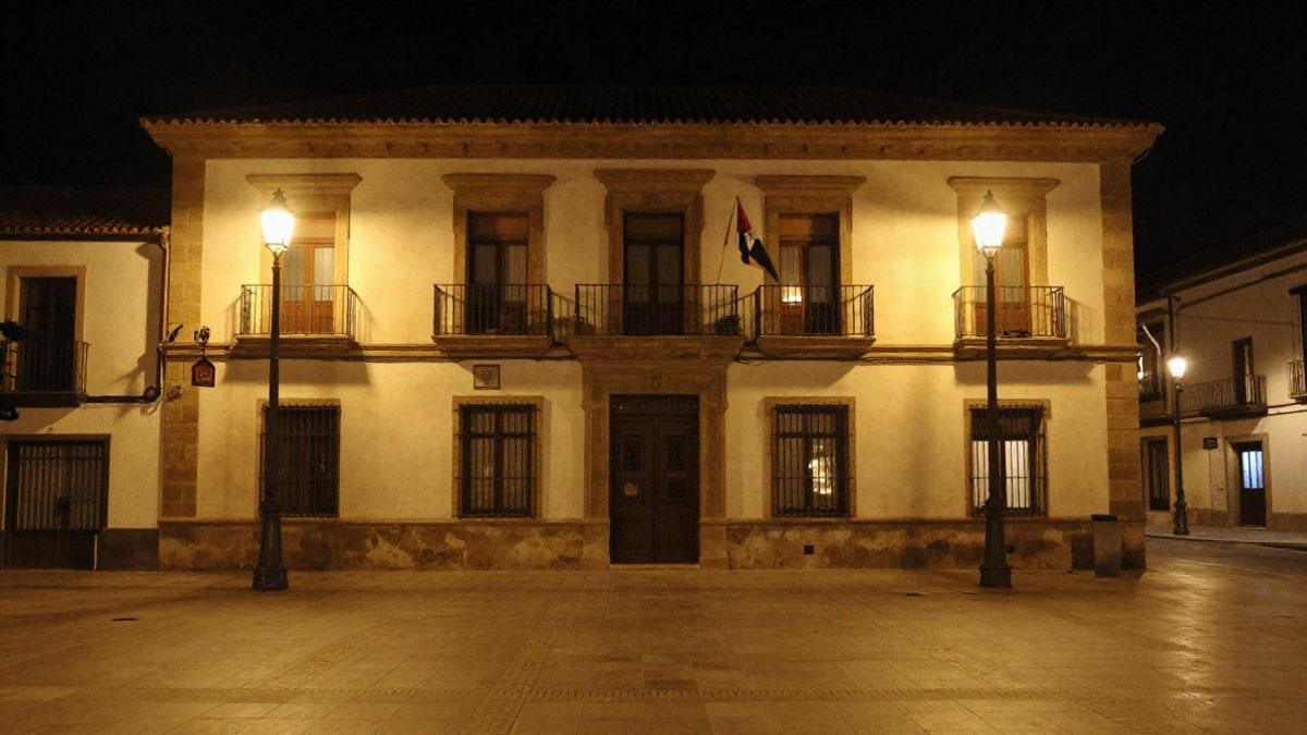 Imagen ilustrativa: fachada de un edificio municipal de noche con farolas encendidas y una plaza vacía