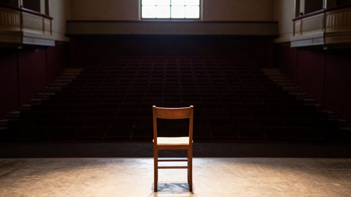 Imagen ilustrativa: un escenario de teatro vacío con una silla iluminada por luz cálida y butacas oscuras al fondo