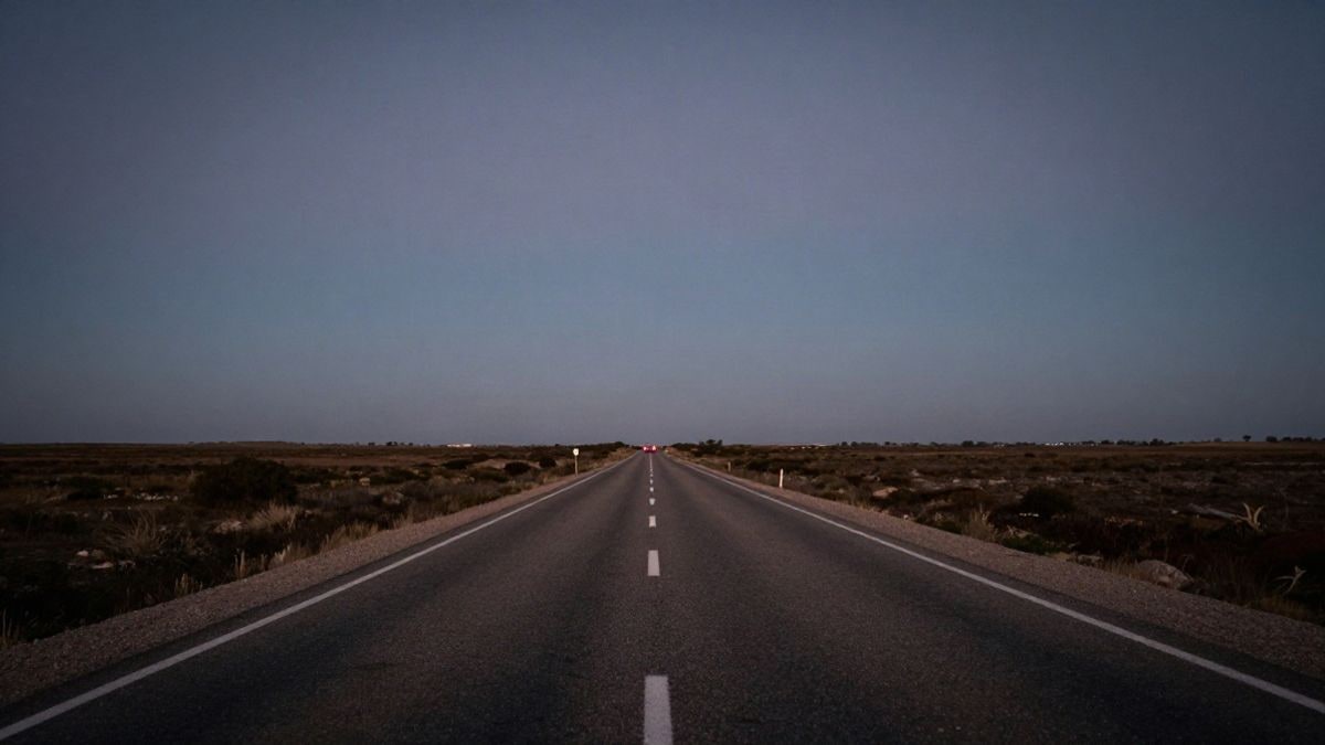 Imagen ilustrativa: carretera rural vacía al atardecer, con las luces traseras de un coche lejano en un paisaje llano