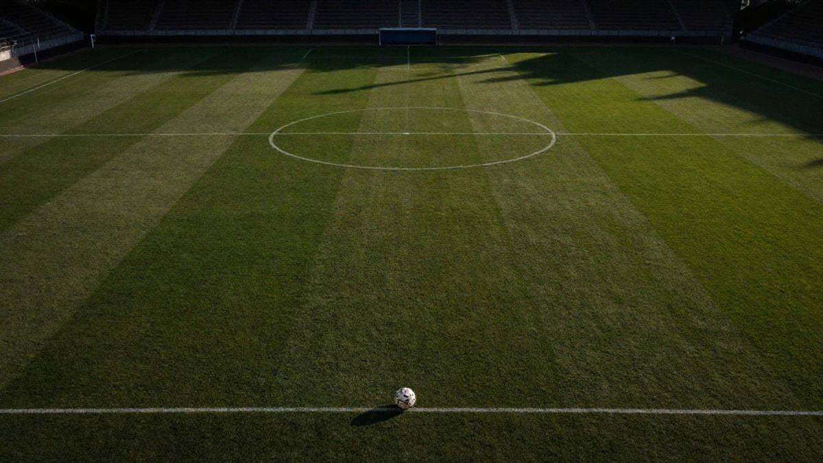 Imagen ilustrativa: vista cenital de un campo de fútbol al atardecer con un balón en el césped