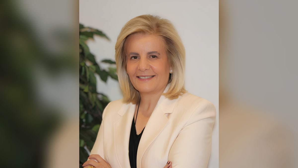 Retrato de Fátima Báñez con chaqueta crema, sonriendo ante una planta verde, en fondo claro