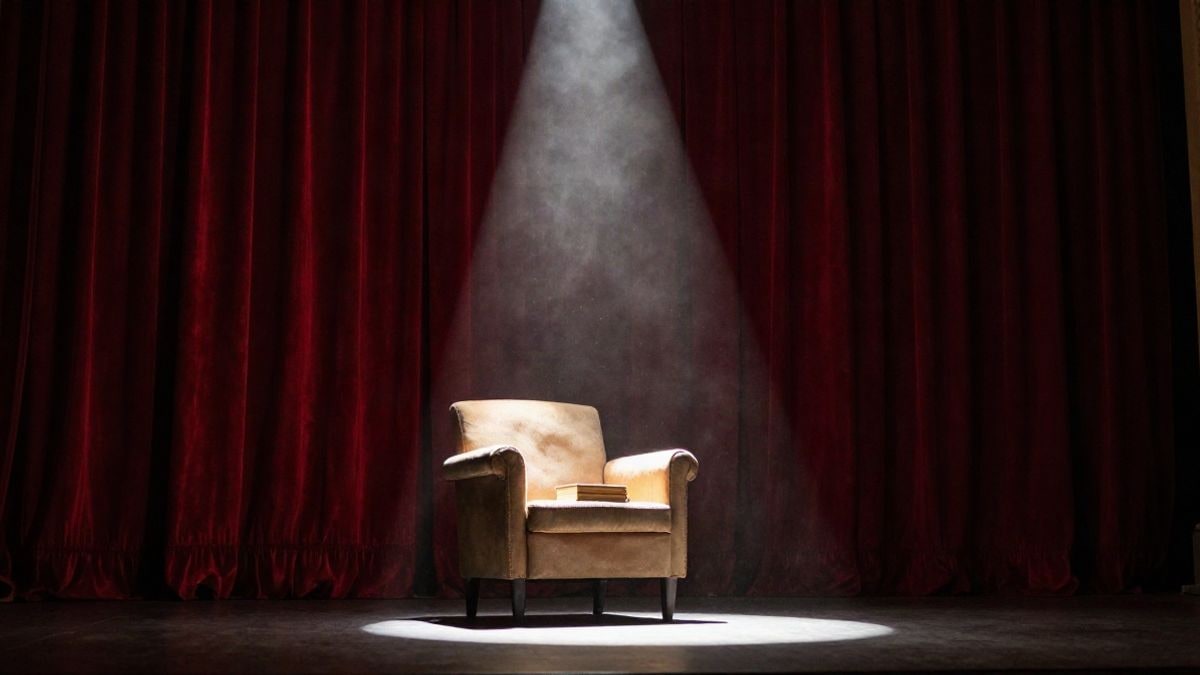 Imagen ilustrativa: un sillón antiguo y un libro sobre un escenario teatral vacío iluminado por un foco