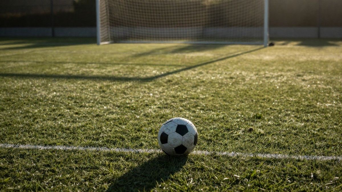 Imagen ilustrativa: un balón de fútbol sobre el césped de un campo al amanecer, con las porterías al fondo