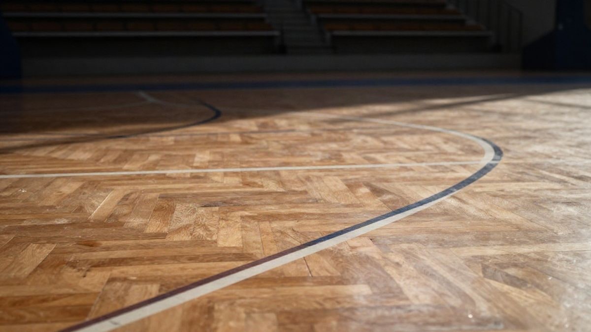 Imagen ilustrativa: detalle de la madera pulida de una cancha de baloncesto con líneas pintadas y luz natural