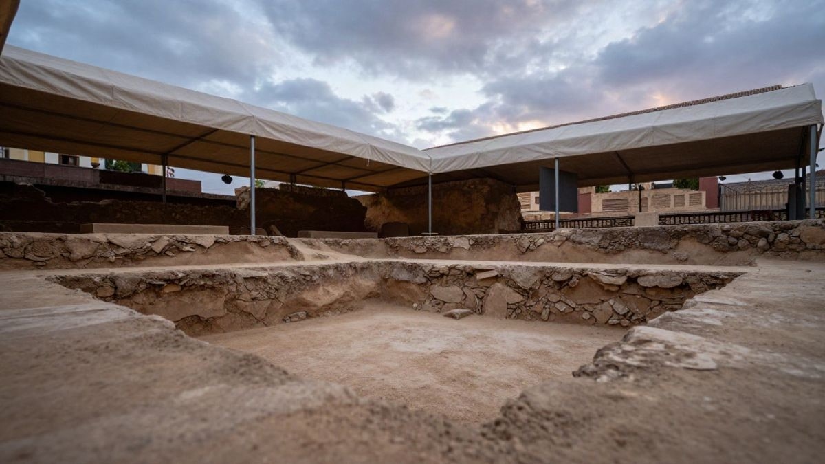 Imagen ilustrativa: ángulo bajo de una excavación arqueológica urbana cubierta por una carpa, con estratos de tierra y cielo al fondo