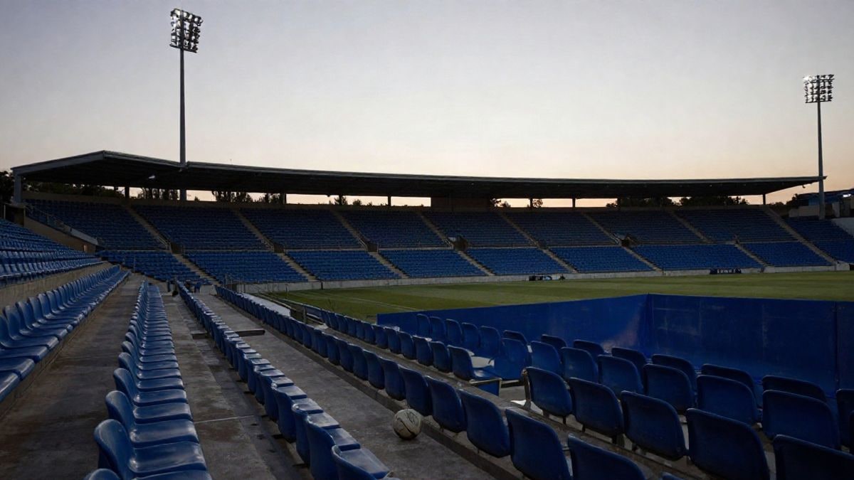 Imagen ilustrativa: gradas vacías de un estadio de fútbol al atardecer con un balón en el pasillo