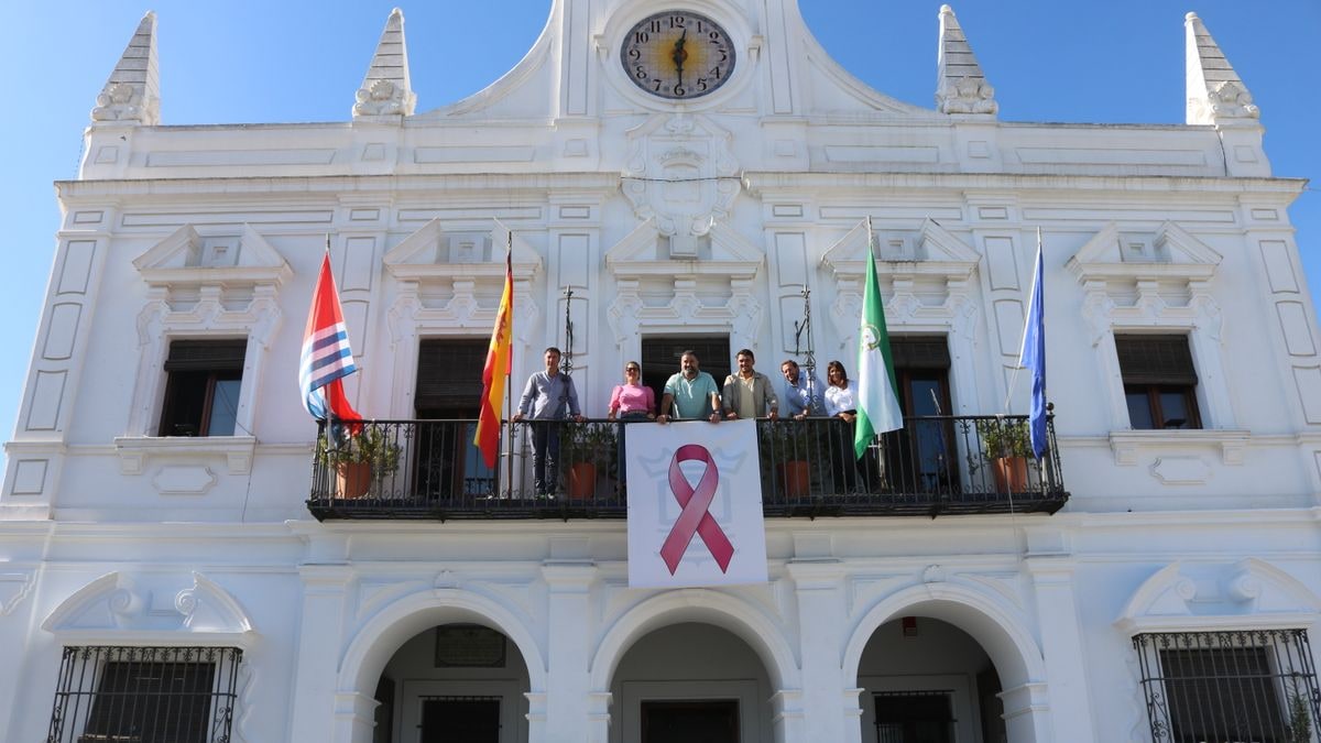 Imagen ilustrativa: lazo rosa colgado en la fachada blanca de un edificio municipal al atardecer