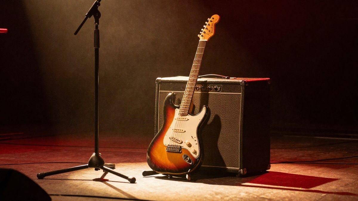 Imagen ilustrativa: guitarra eléctrica apoyada en un amplificador en un escenario con luces cálidas