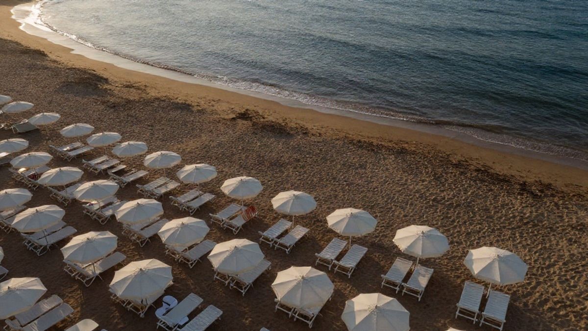 Imagen ilustrativa: vista cenital de una playa con sombrillas y tumbonas vacías al atardecer