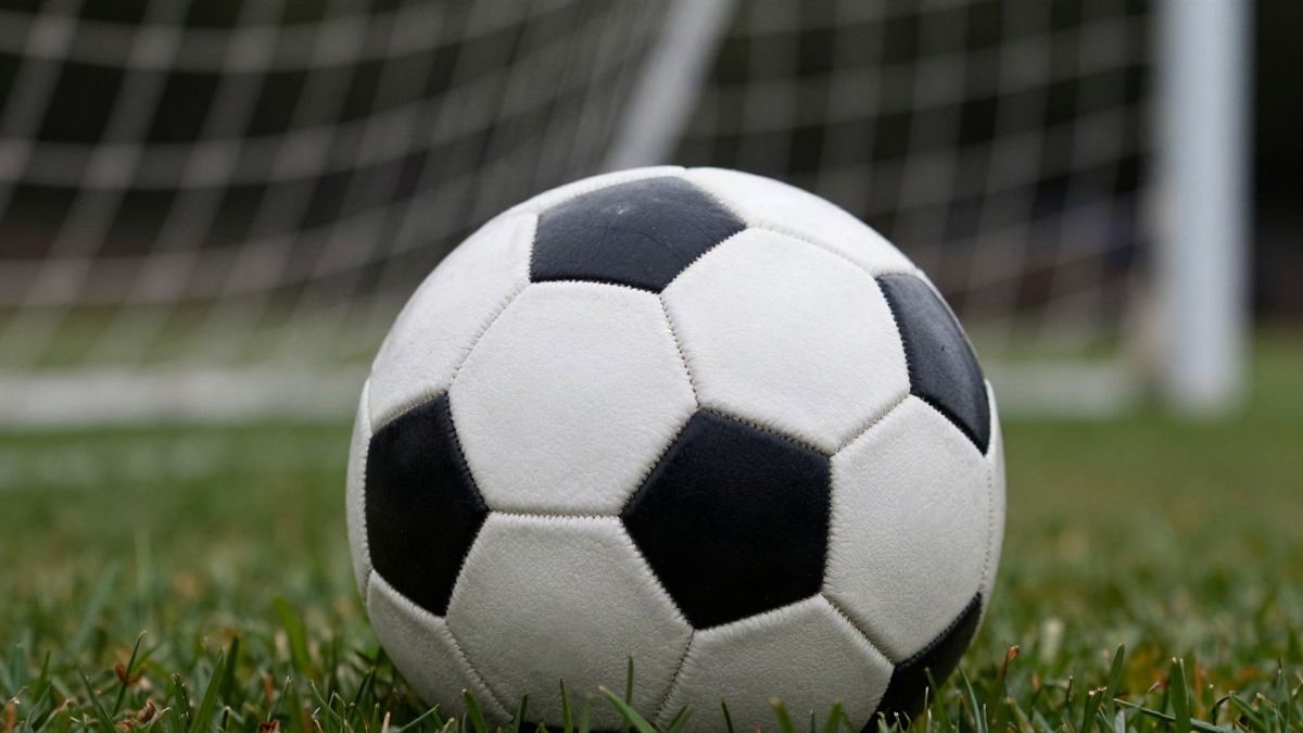 Imagen ilustrativa: primer plano de un balón de fútbol sobre el césped con una portería desenfocada al fondo