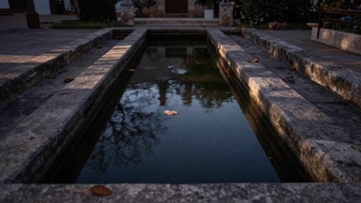 Imagen ilustrativa: agua estancada en una pila de piedra antigua al atardecer, con sombras largas en un jardín