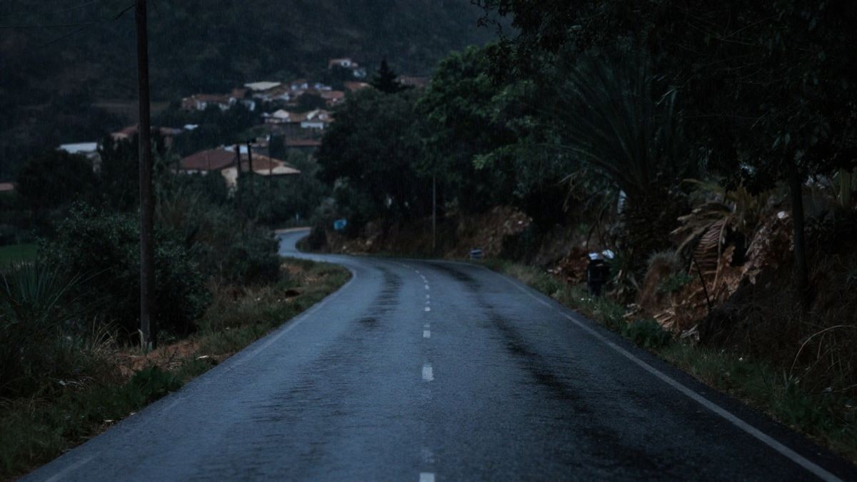 Imagen ilustrativa: una carretera rural oscura y mojada por la lluvia, con un vehículo detenido y una figura borrosa de espaldas en la distancia.